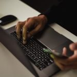 crop faceless man typing on laptop and using smartphone